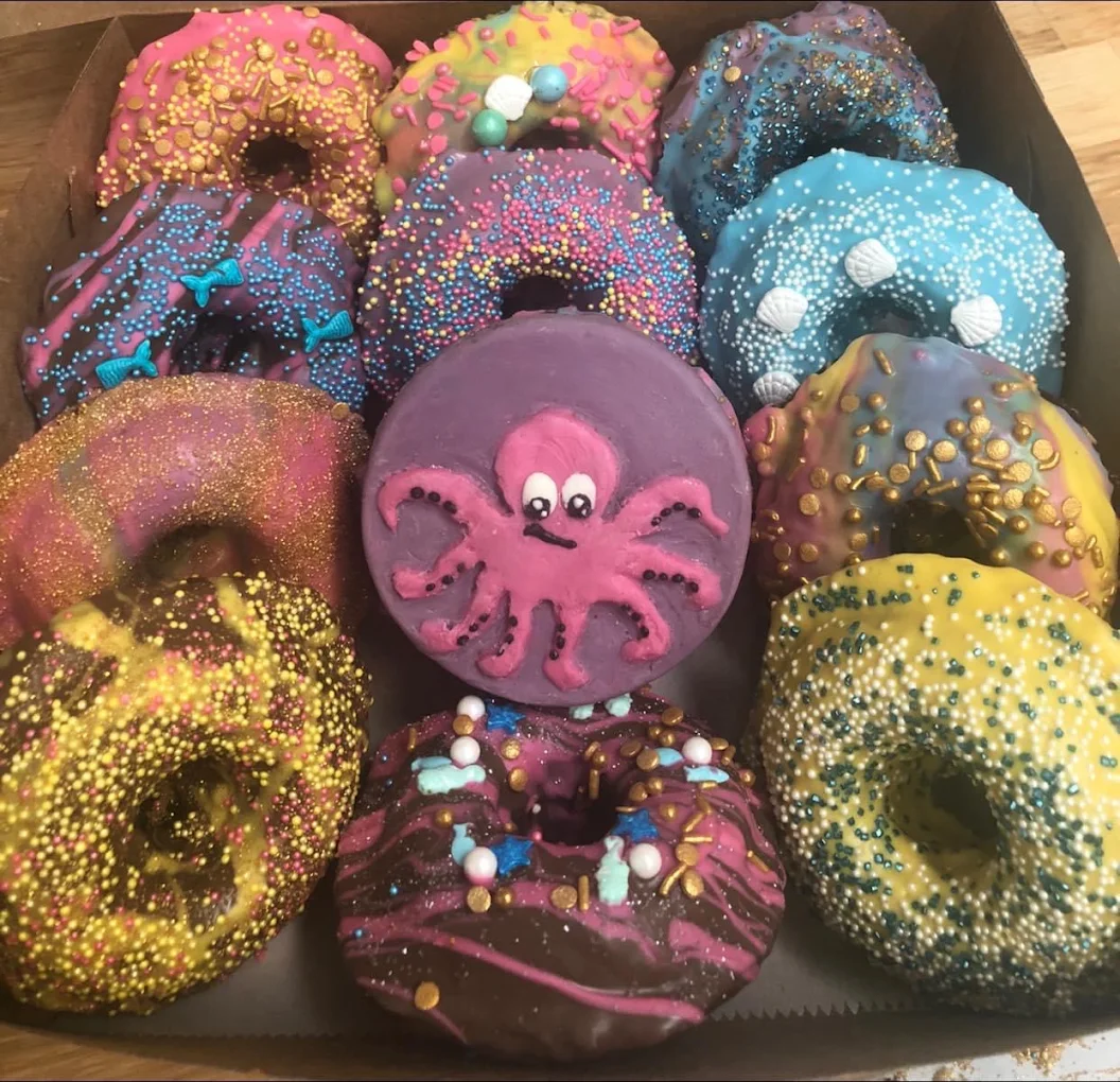 A box of wildly colorful decorated donuts with a pink octopus centerpiece